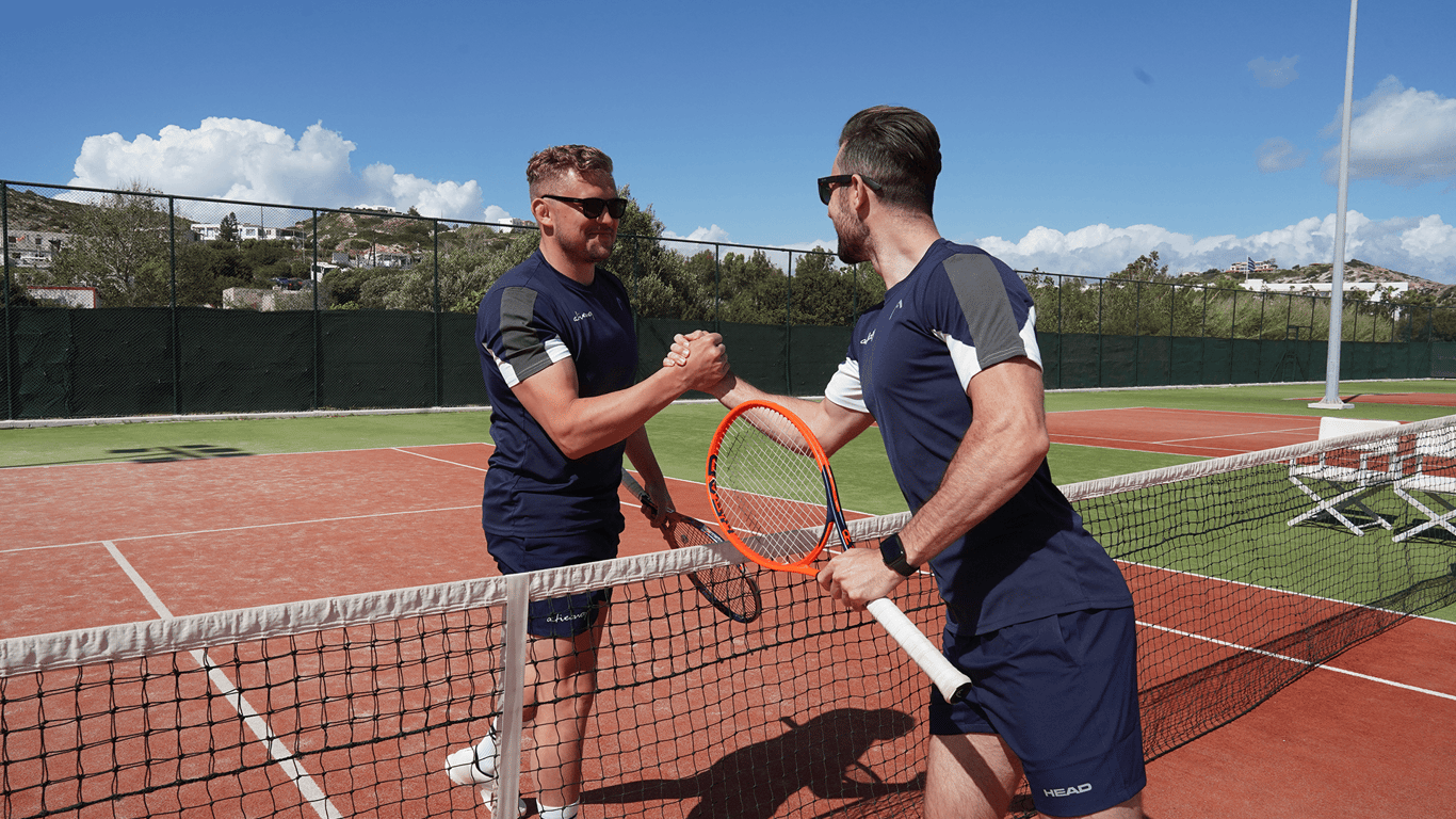 Two players shake hands over the net on a sunny tennis court after a match.