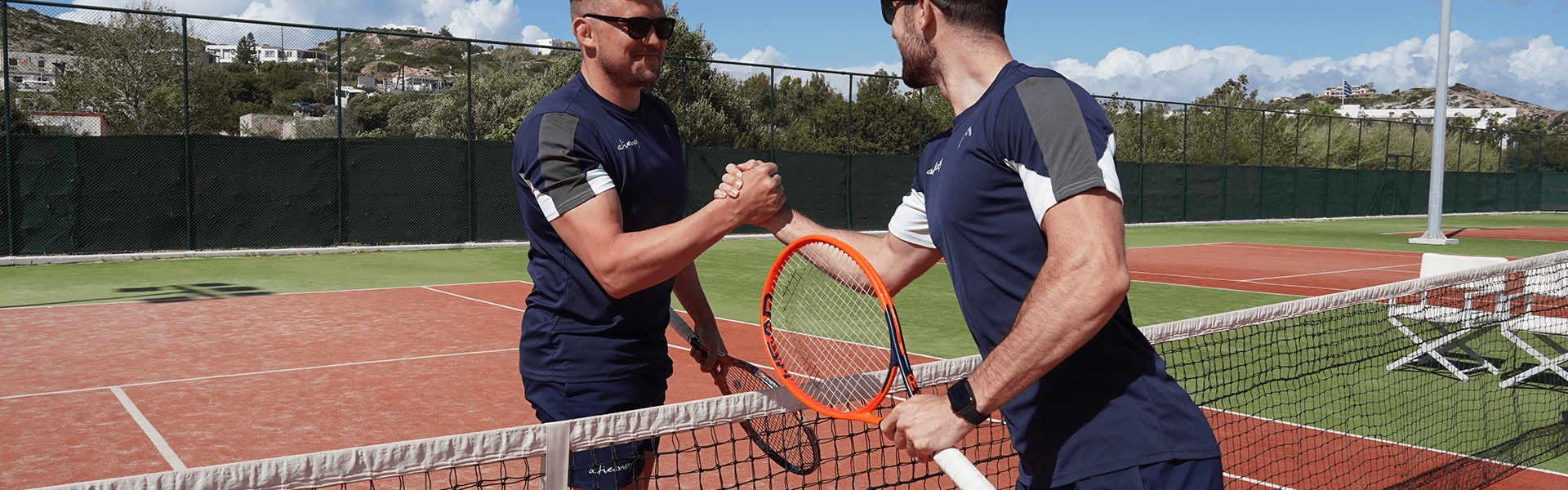 Two players shake hands over the net on a sunny tennis court after a match.