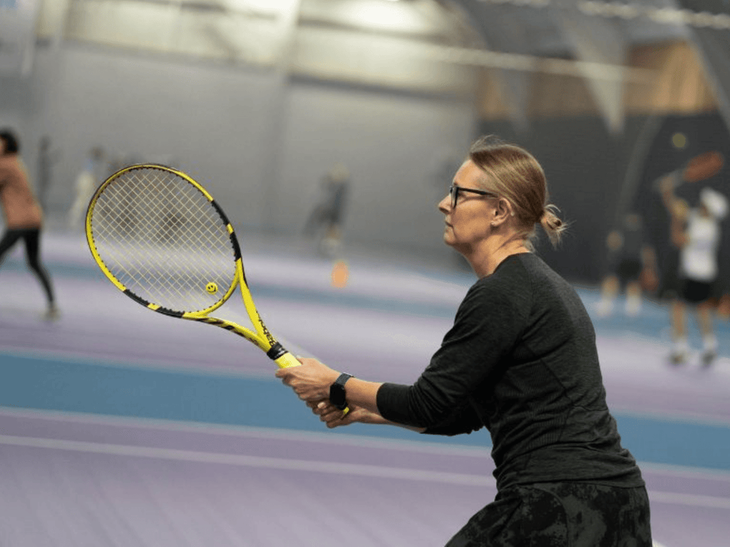 Woman in ready position holding a yellow tennis racket on an indoor court.