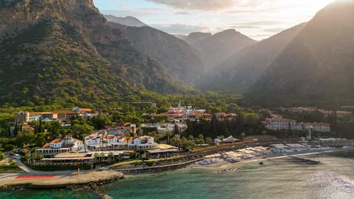 Coastal resort beneath forested mountains with beaches and red‑roofed buildings at sunset.