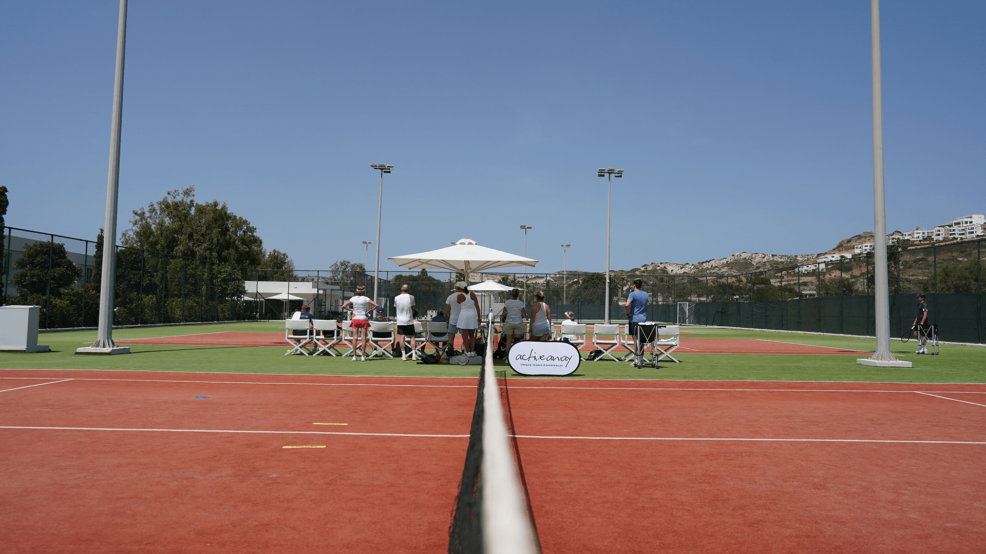 Tennis coaching group on a sunny outdoor court, viewed along the centre net.