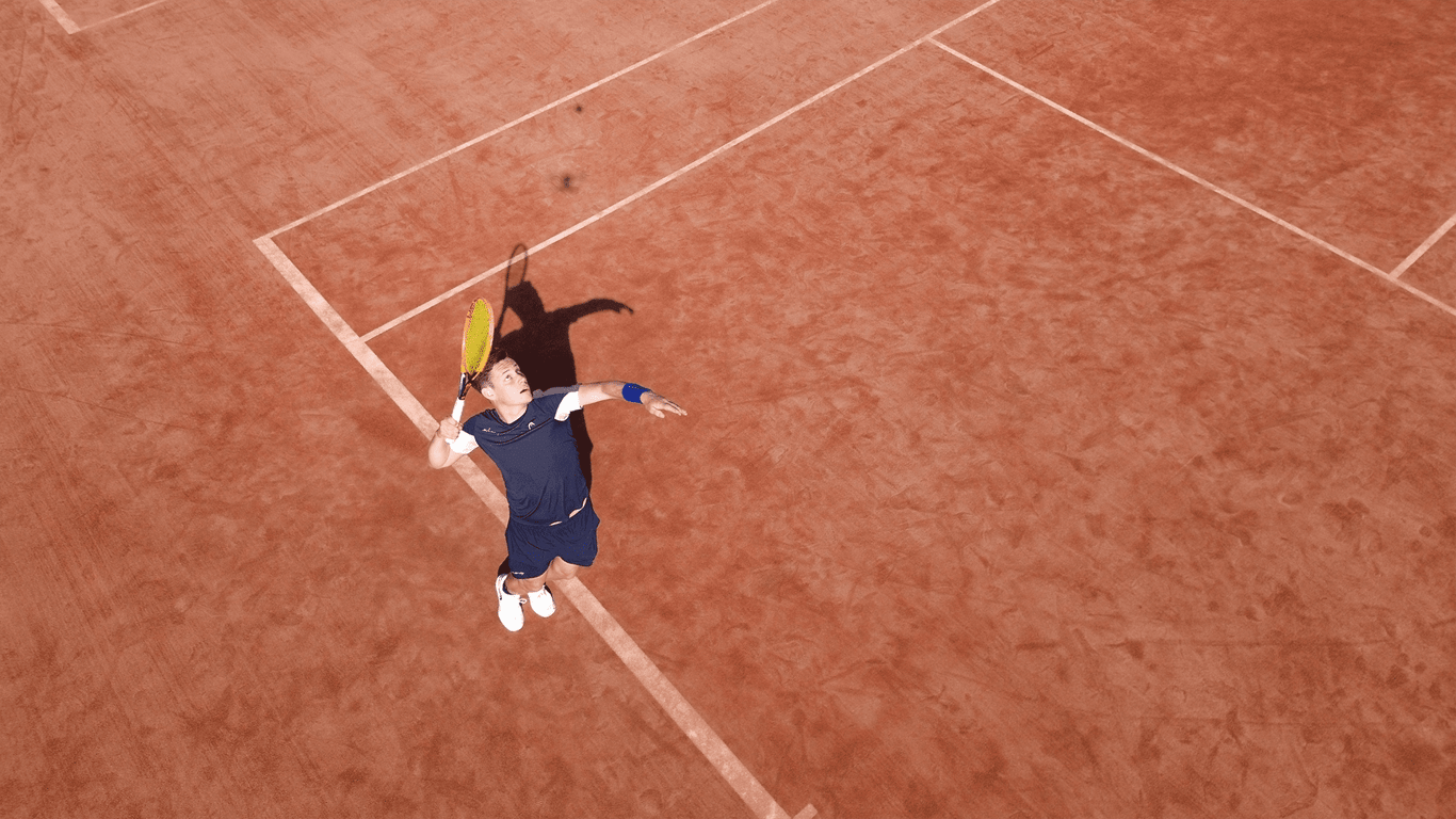A tennis player leaping to serve on a clay court, seen from above.