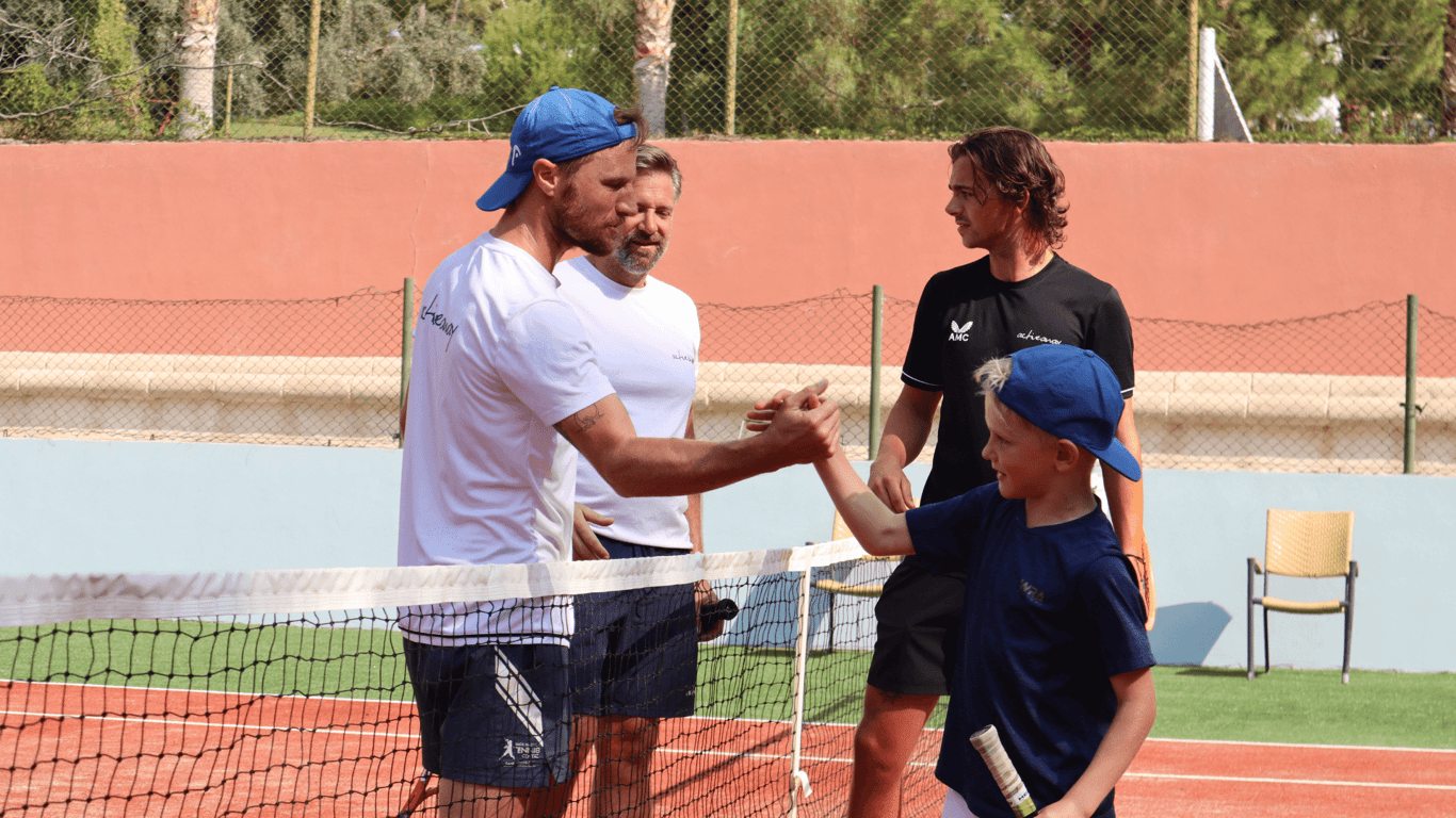 Coach high-fives a young player over a tennis net during a holiday coaching session.