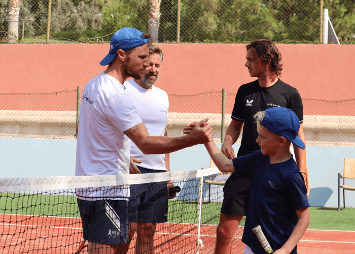 Coach high-fives a young player over a tennis net during a holiday coaching session.