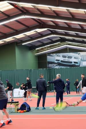 Indoor tennis coaching session with instructor guiding players on a court.