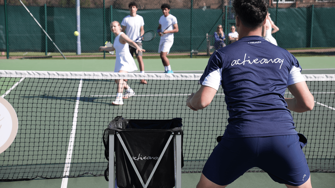 Coach leads junior tennis drill as players practise at the net during an Active Away camp.