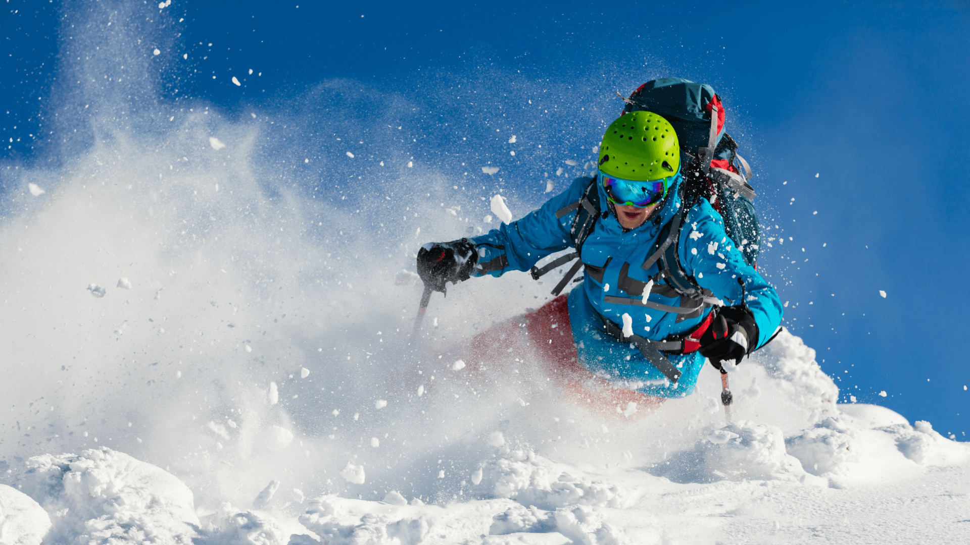 Skier carving through deep powder, snow spraying into the air under a clear blue sky.