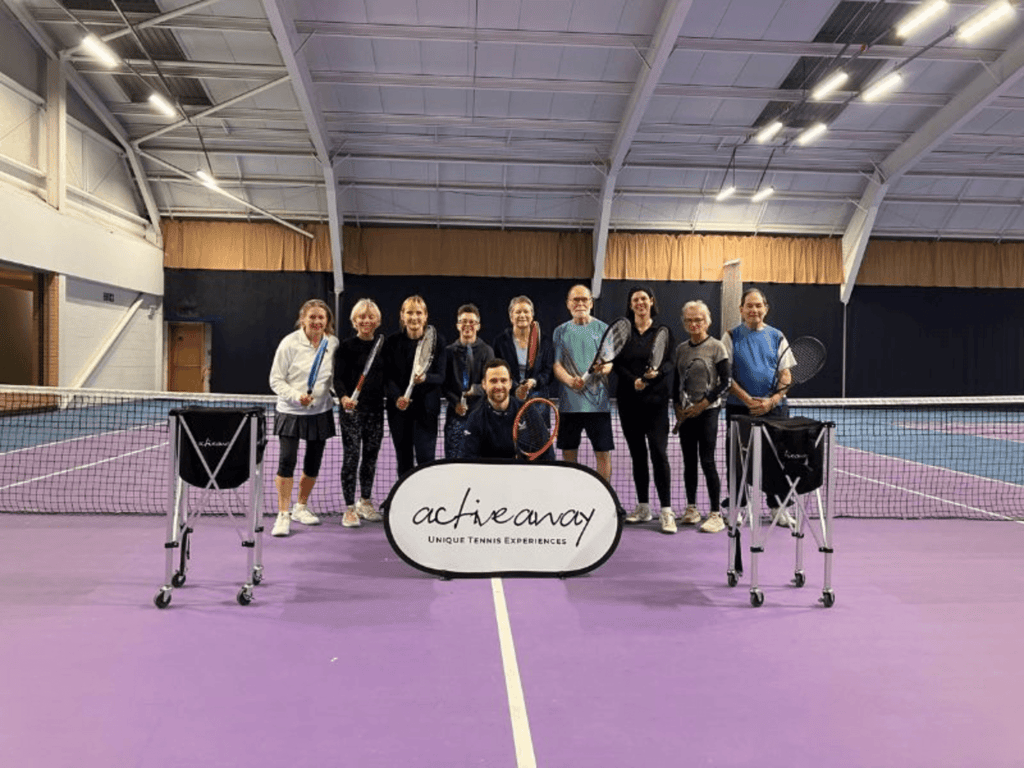 Group of tennis players on an indoor court holding rackets beside an Active Away sign.