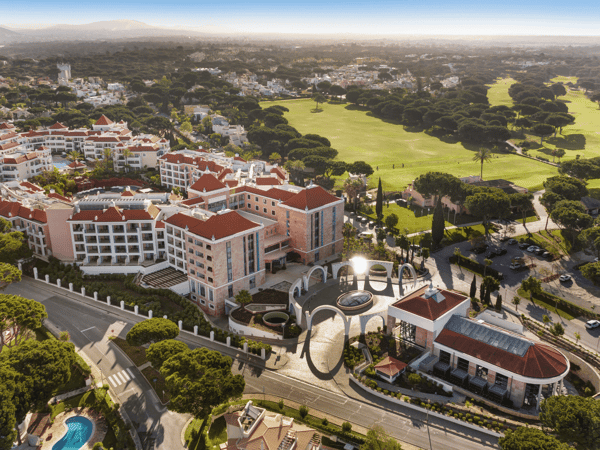 Aerial view of a luxury Mediterranean resort beside a golf course, with red-tiled roofs and pools.