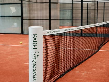 Brand deck mock-up of a Padel Tropicana branded net across a terracotta padel court.