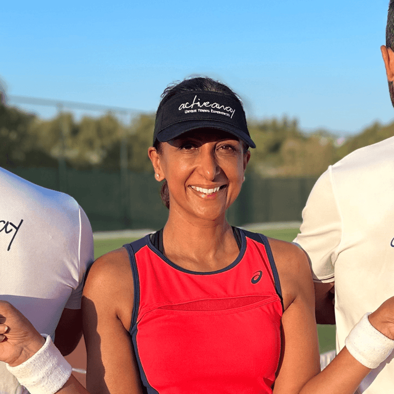 Smiling woman in red top wearing an Active Away visor on a sunny tennis court.