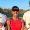 Smiling woman in red top wearing an Active Away visor on a sunny tennis court.