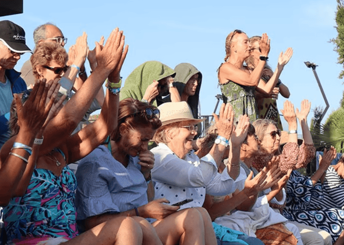 Crowd of holiday clients clapping and cheering courtside at a sunny tennis event.