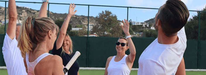 Group of adults on a tennis court raising hands in a team cheer during a coaching session.