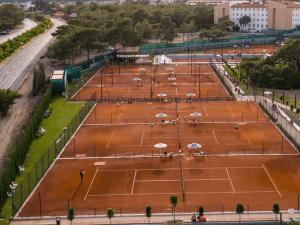 Aerial view of multiple clay tennis courts with players and parasols at a resort.