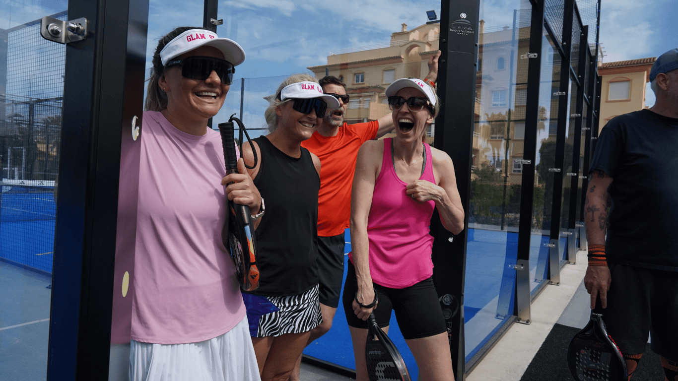 Group of padel players laughing with rackets beside the court during a sunny break.