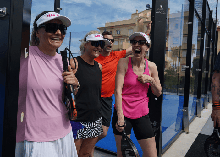 Group of padel players laughing with rackets beside the court during a sunny break.