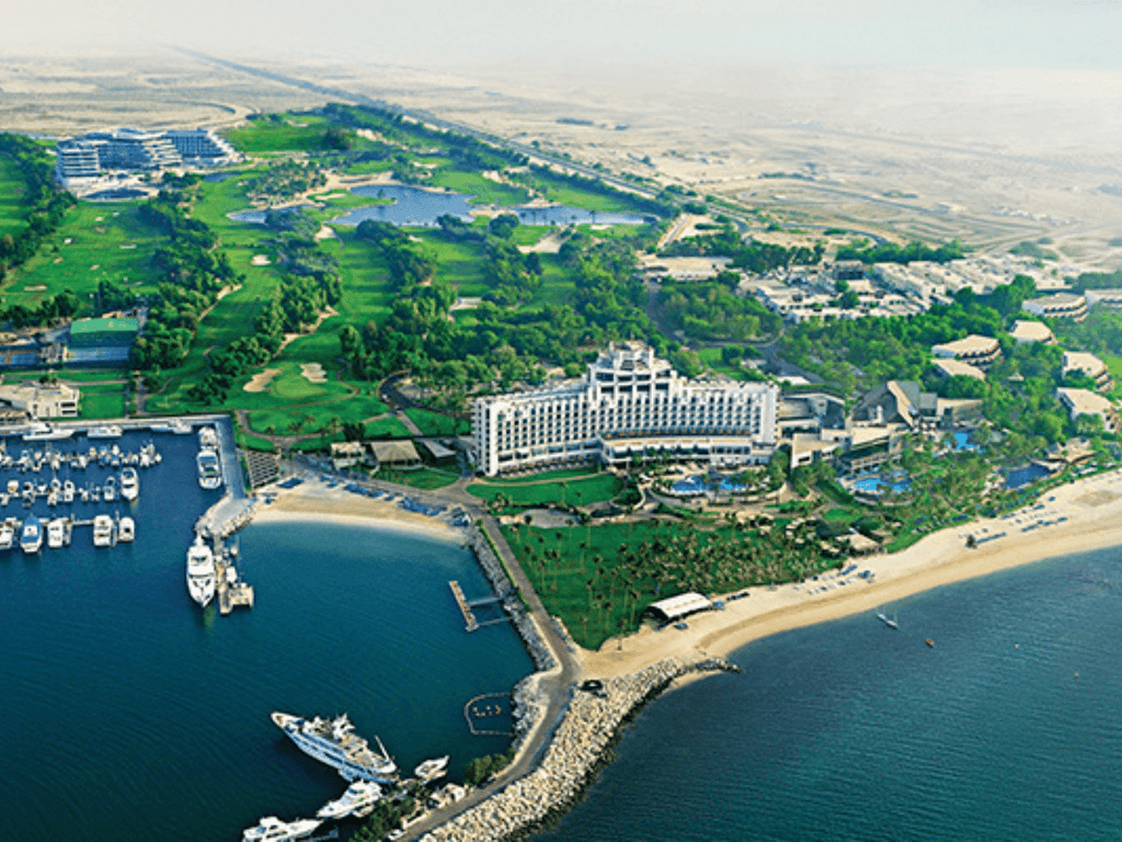 Aerial view of a beachfront resort with marina, golf course, pools and sandy beach.