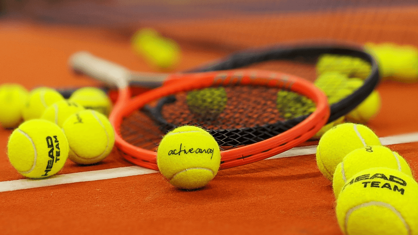 Tennis balls and rackets on a clay court, including an Active Away branded ball.
