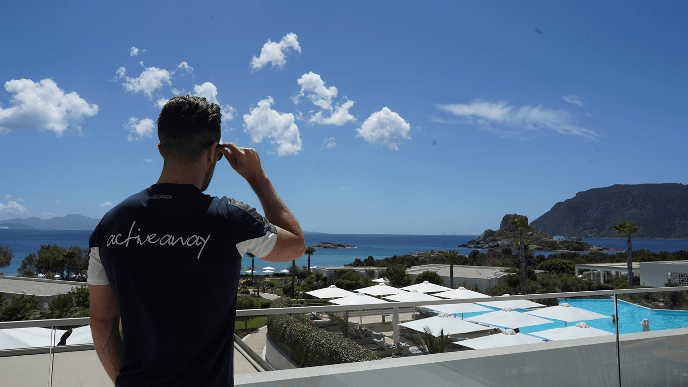 Man in Active Away shirt looking over a seaside resort with pool and mountains on a sunny day.