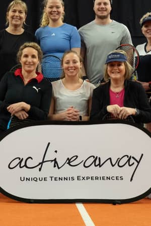 Group of tennis players on indoor court with Active Away sign, featuring nine women and one man holding tennis racquets.