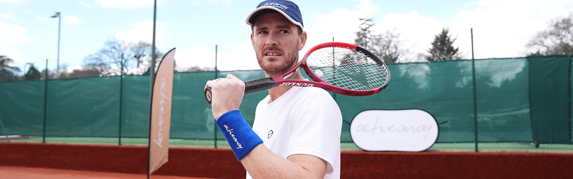 Tennis player on a clay court holding a racket over his shoulder at an Active Away clinic.