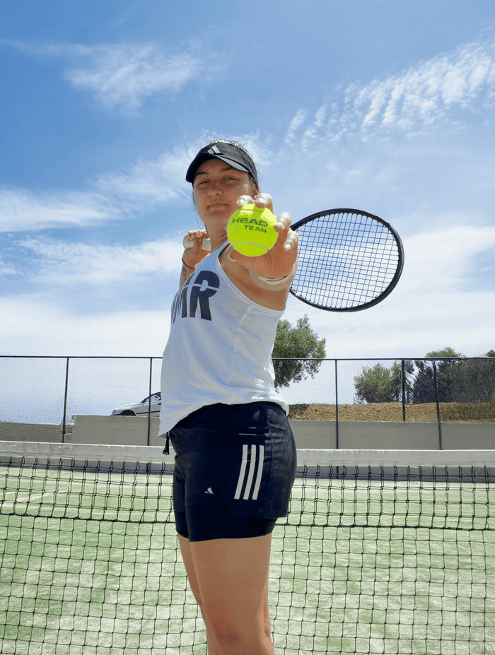 Close-up of a tennis player presenting a ball to the camera, racquet in hand, on an outdoor court.
