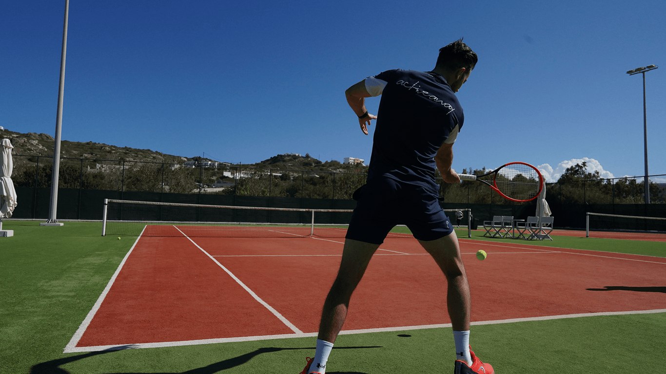 Tennis player in navy kit striking a forehand on a sunny outdoor court.