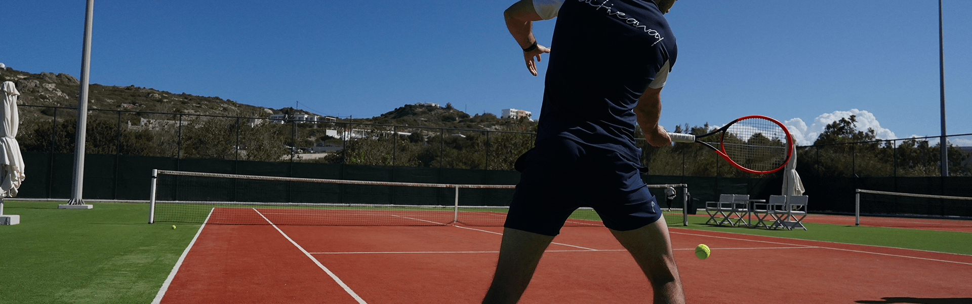 Tennis player in navy kit striking a forehand on a sunny outdoor court.