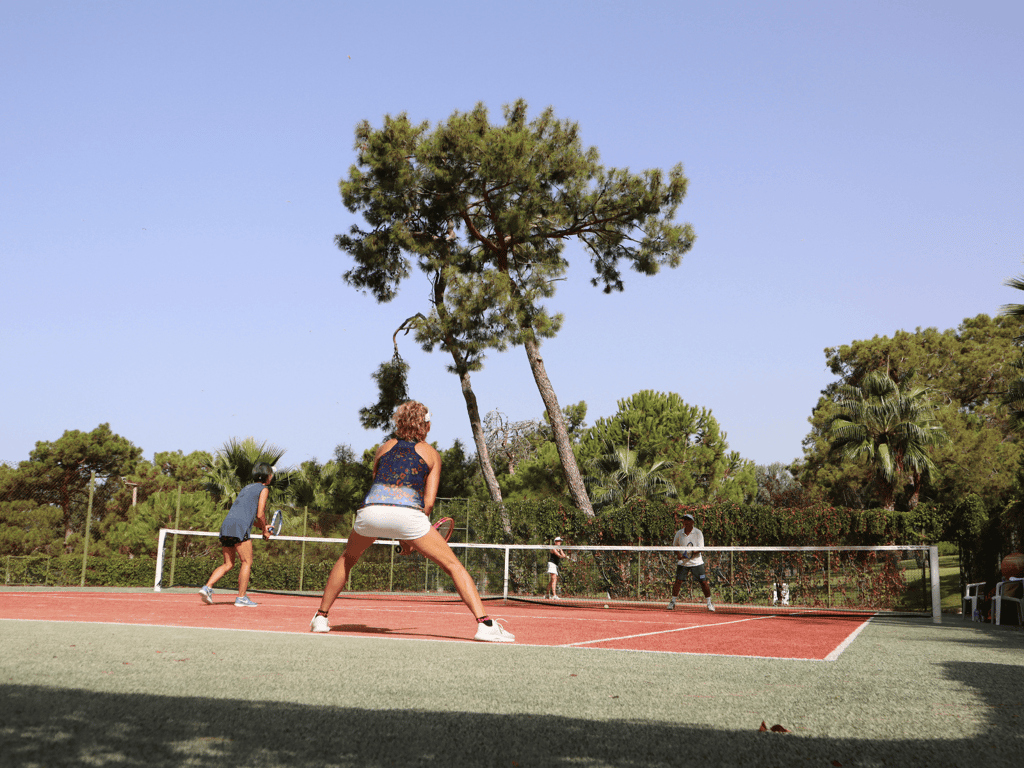 Four adults playing doubles tennis on an outdoor court surrounded by trees.