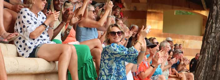 Smiling spectators in summer clothes clap on stone terraces at an outdoor match.