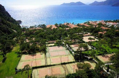 Aerial view of a seaside resort with multiple tennis courts overlooking a blue bay.