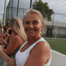 Smiling woman in a white vest cheering courtside during a tennis or padel holiday.