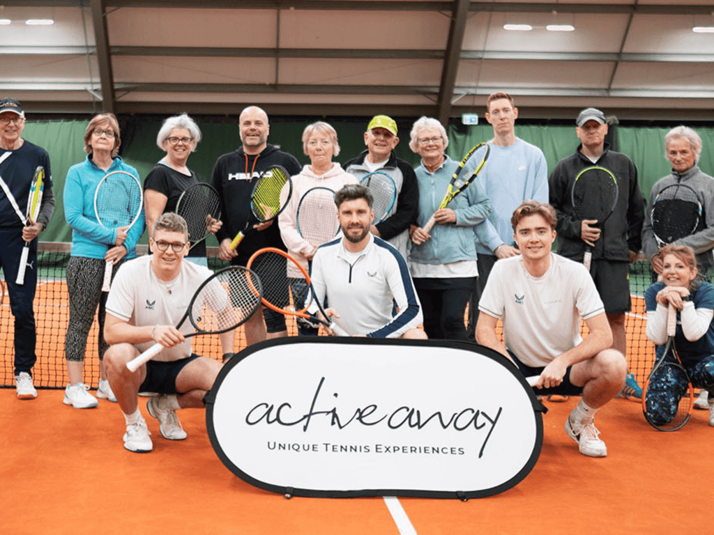 Group of tennis players with rackets on an indoor court behind an Active Away banner.