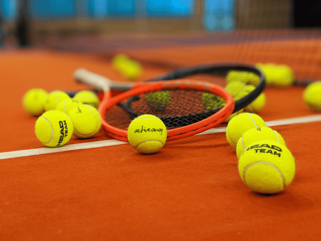 Tennis balls and rackets scattered on a clay court, with an Active Away ball in focus.