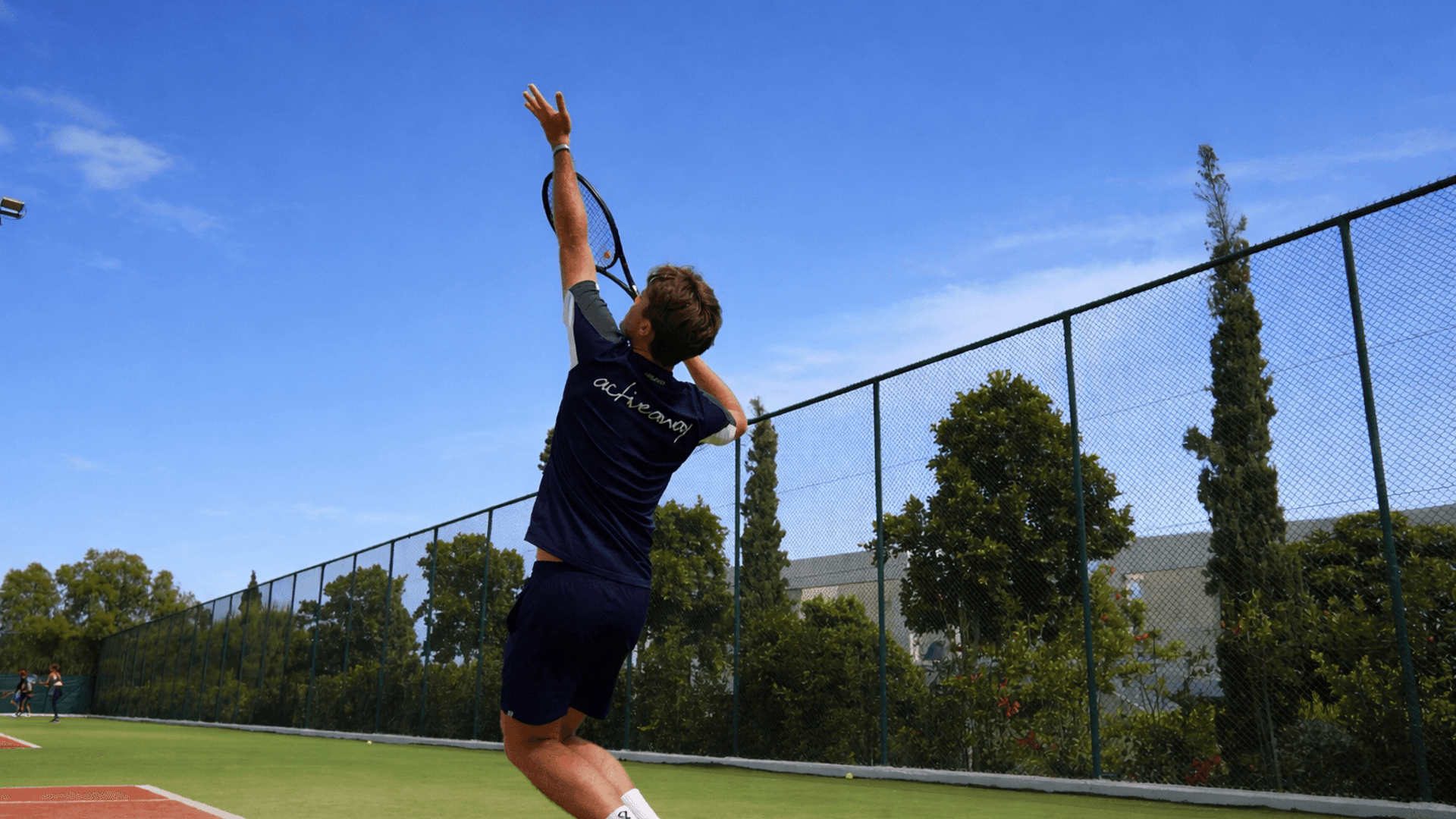 Tennis player jumping to serve on an outdoor court under a blue sky.