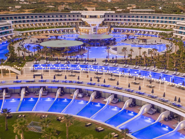 Aerial view of a luxury resort with sweeping pools and sun loungers at dusk.