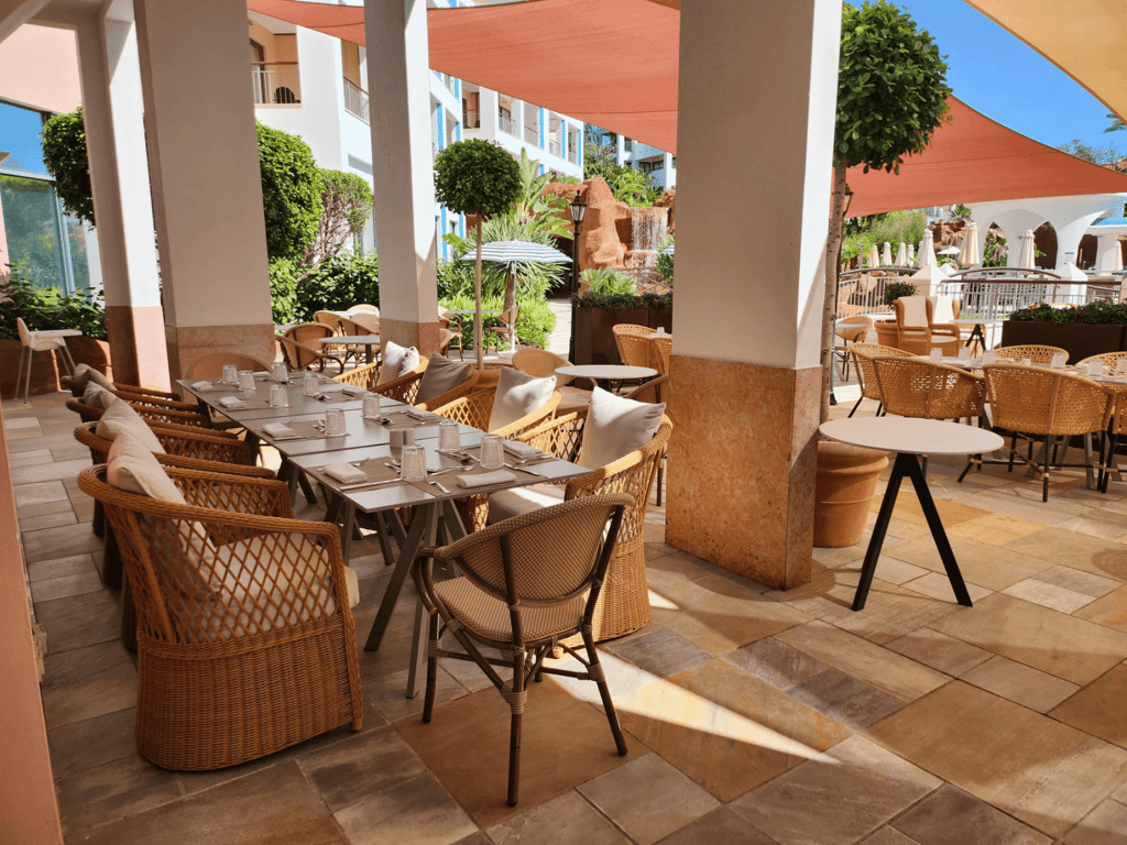 Shaded resort terrace with wicker chairs and set tables for outdoor dining.