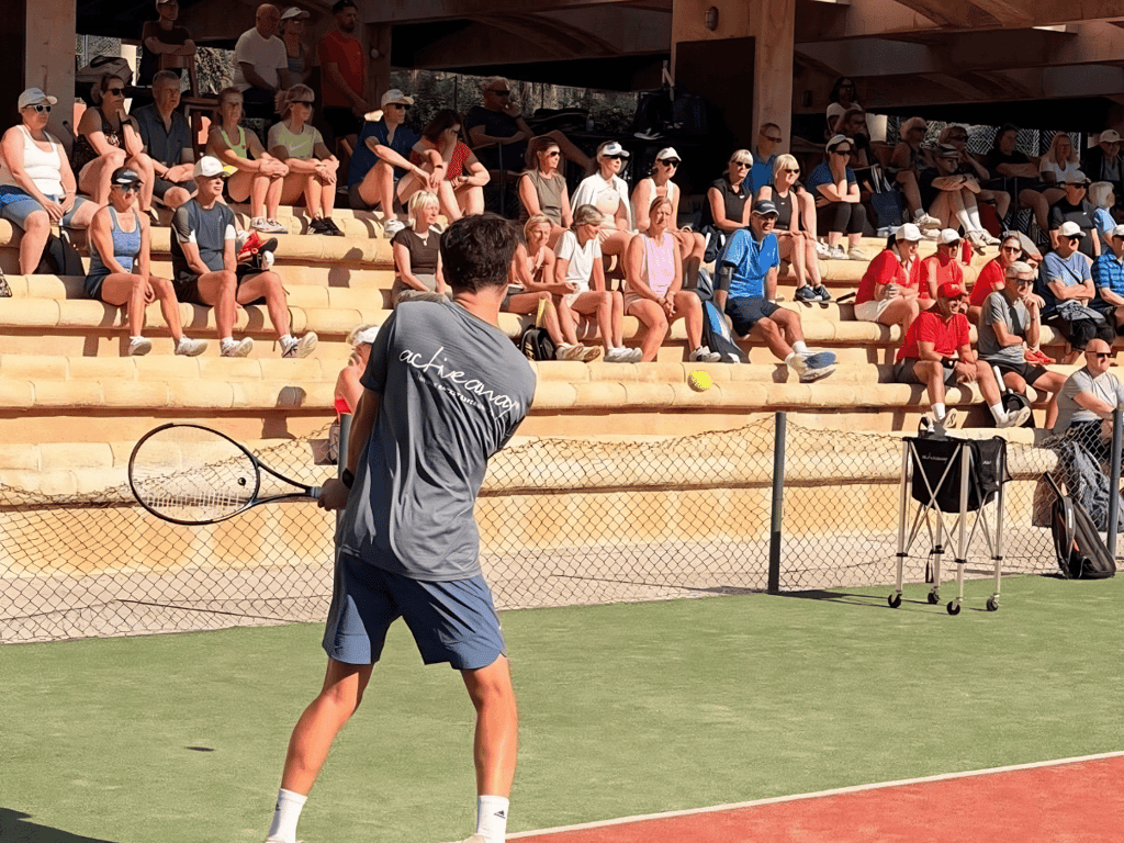 Tennis coach demonstrates a shot to a full crowd on stone bleachers during an Active Away clinic.