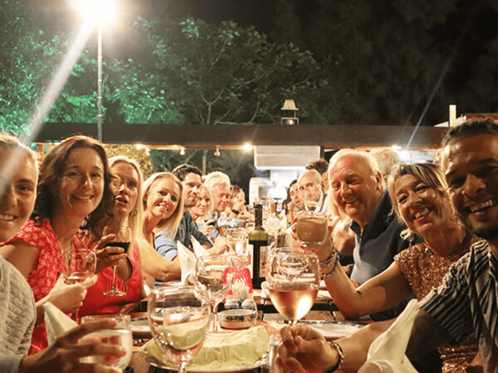 Large group toasting with drinks at a long outdoor dinner table during an Active Away holiday evening.