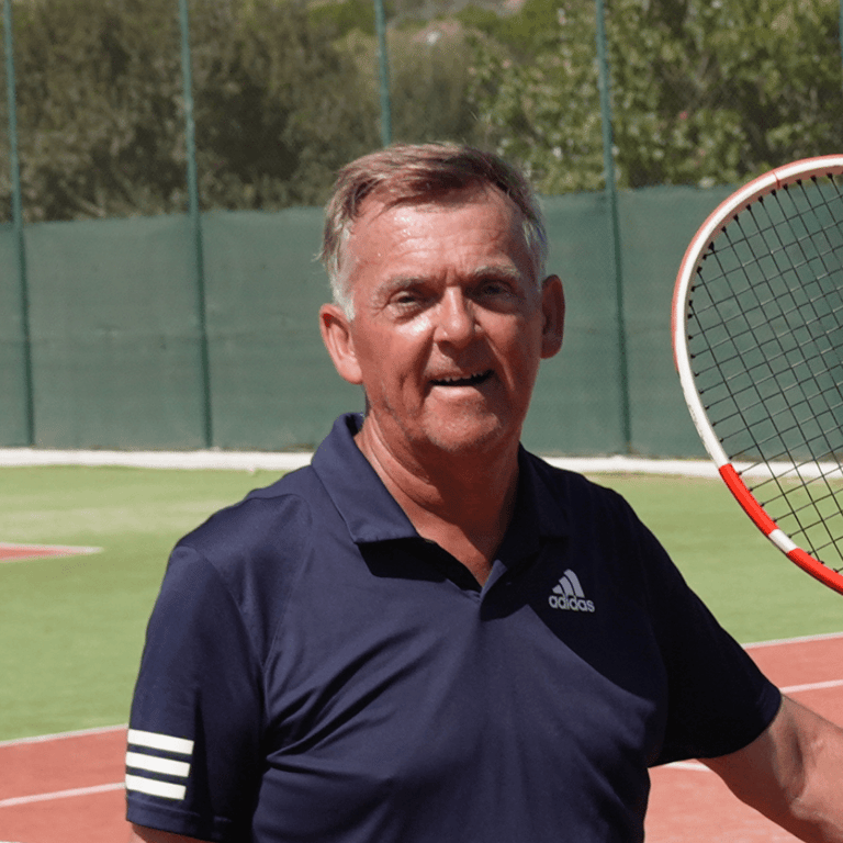 Smiling player on a sunny outdoor tennis court holding a racquet, wearing a navy adidas polo.