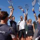 Active Away tennis group raising rackets together on a sunny court.