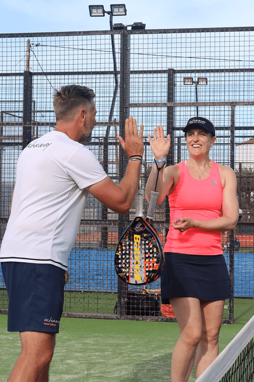 Two padel players high-five on court, smiling after a point.