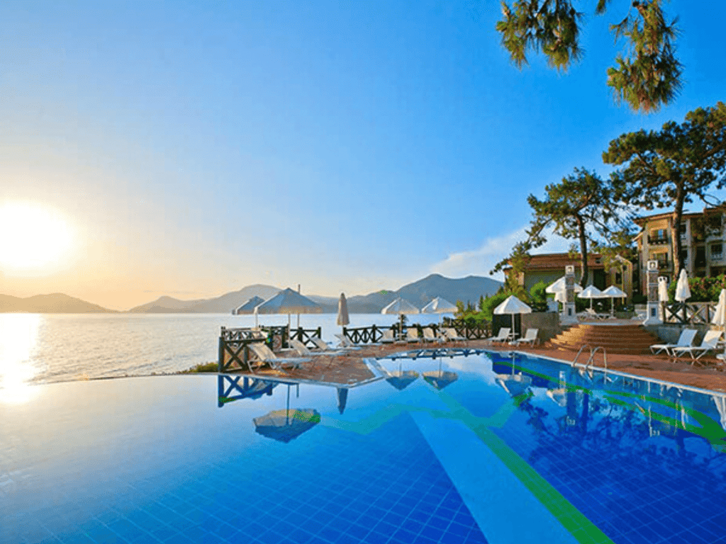 Sunset over a coastal resort with infinity pool, loungers and umbrellas by the sea and mountains.
