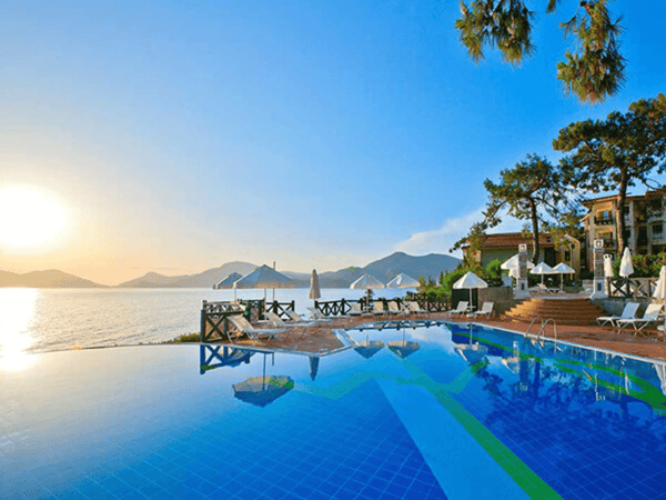 Sunset over a coastal resort with infinity pool, loungers and umbrellas by the sea and mountains.