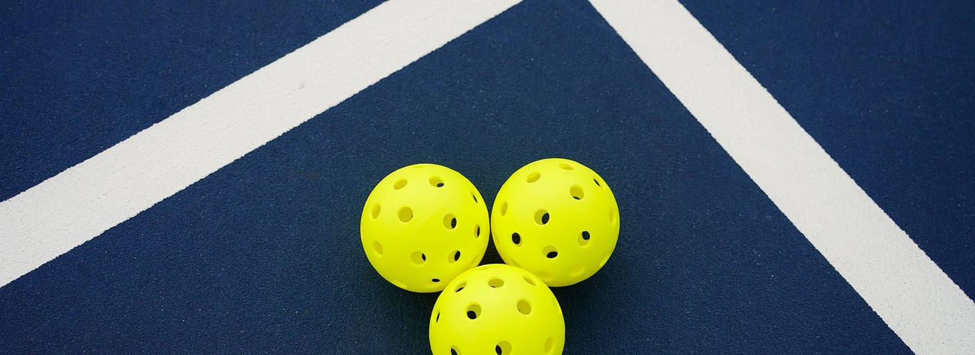 Three yellow pickleballs on a blue court with intersecting white lines.
