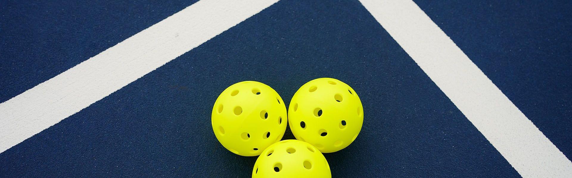 Three yellow pickleballs on a blue court with intersecting white lines.