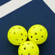 Three yellow pickleballs on a blue court with intersecting white lines.
