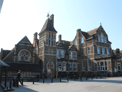 Historic brick school building with clock tower and courtyard under clear sky.