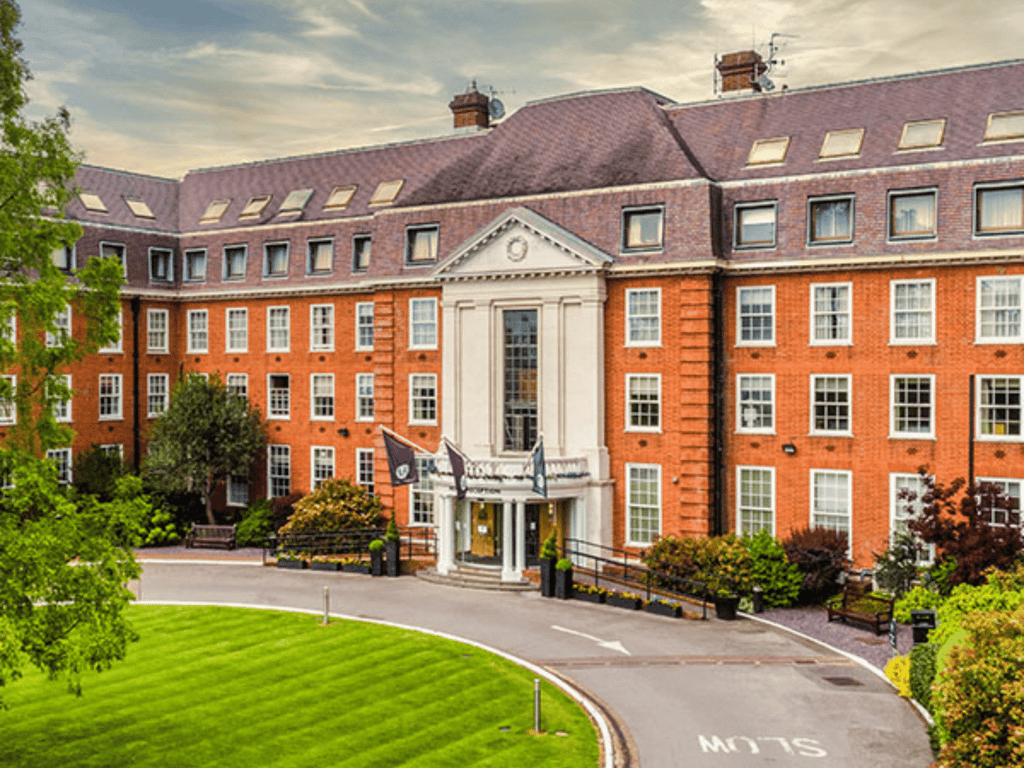 Red-brick hotel with grand portico, curved driveway and manicured lawns